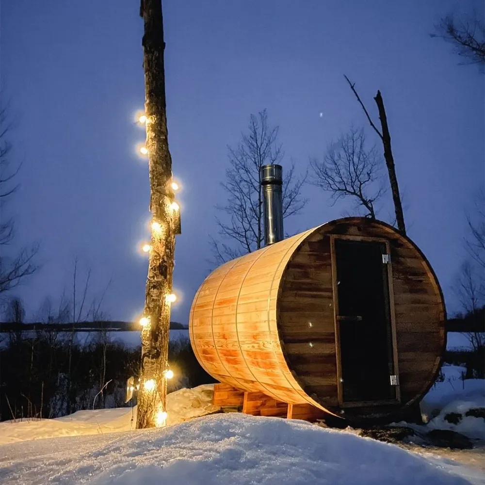 ignis dome outdoor dry sauna with outdoor string hanging lights wrapped around a tree during the winter season in the evening with snow the ground