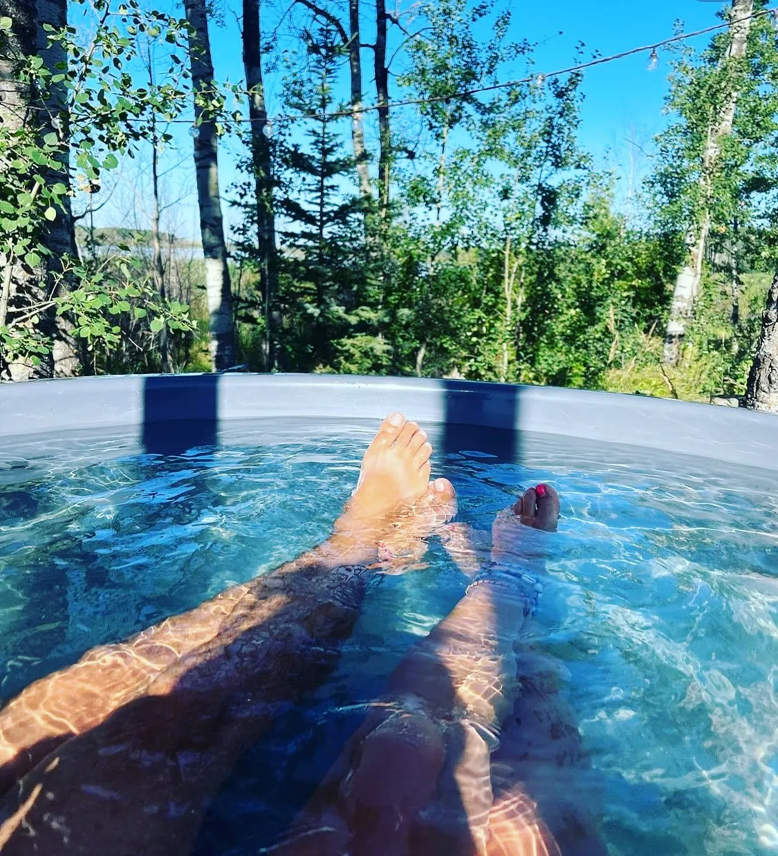 A couple's legs and feet sitting inside the outdoor hot tub having a relaxing time during the summer with forest views