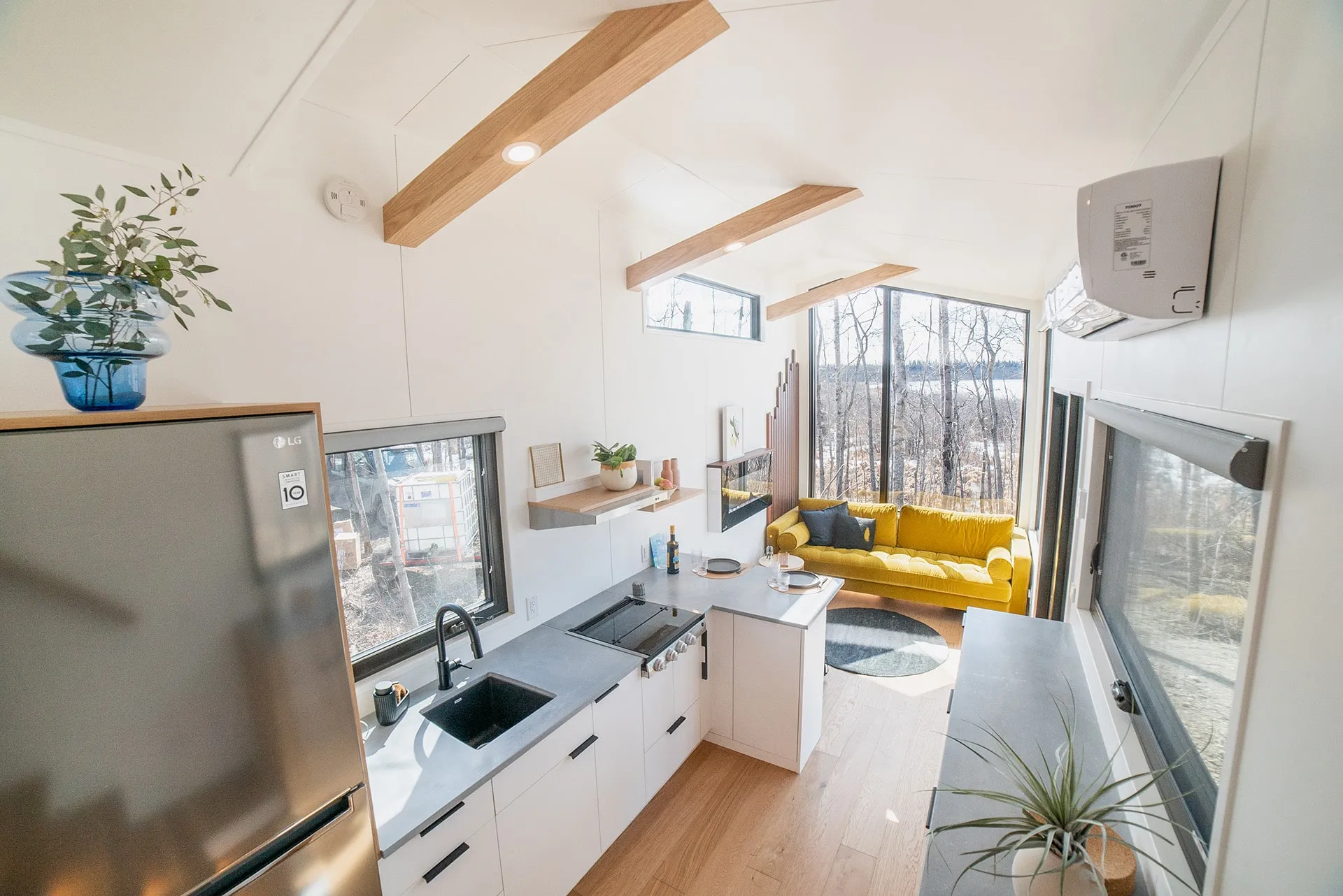 angled view of aqua tiny homes living room space on the main floor with modern kitchen in a small space featuring a yellow couch and a floating fireplace